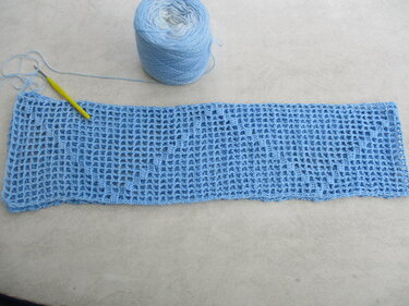 Hellblauer gehäkelter Loop im offenen Netzmuster mit Garnknäuel und gelber Häkelnadel