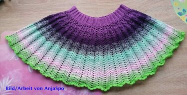 Gehäkelter Kinderrock in Violett, Mint und Grün mit Wellen- und Muschelkante, flach auf Holzuntergrund.