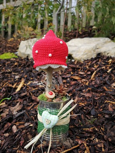 Roter gehäkelter Pilz mit weißen Pünktchen in dekorierter Blechdose auf Rindenmulch