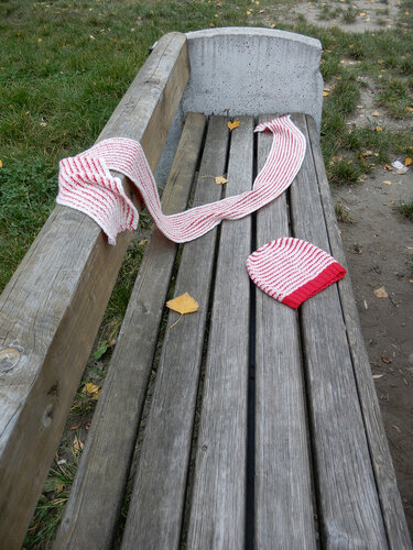 Women's pink and white striped beanie with red cuff and matching long scarf on a wooden bench