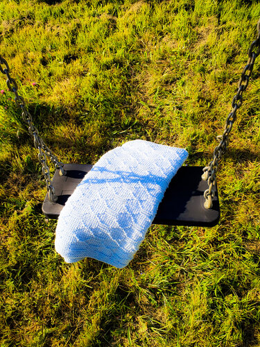 Zarte hellblaue Babydecke gefaltet auf einer Schaukel im sonnigen Gras