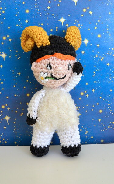 Gehäkelte Amigurumi-Puppe mit gelben Hörnern, schwarzer Mütze und Blume im Mund