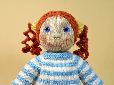 Hand-knitted doll with red curly pigtails and a blue-and-white striped sweater.