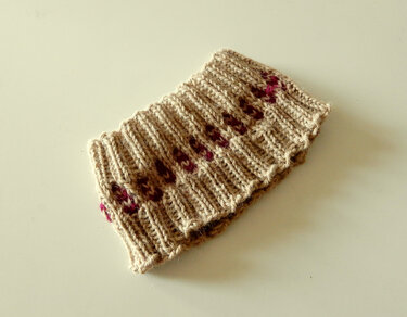 Beige knitted headband with small pink accent stitches on a neutral background.