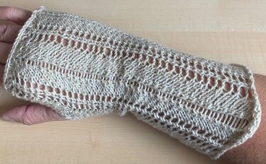 Fingerlose gestrickte Armstulpe in Hellbeige mit Ajourmuster und Daumenöffnung, getragen