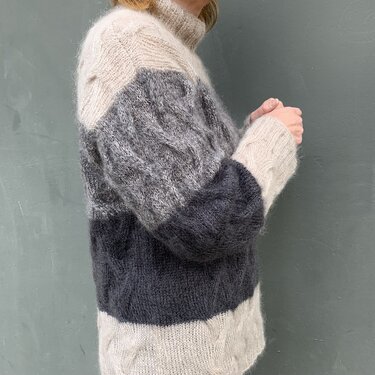 Nahaufnahme eines Damenpullovers mit Zopfmuster, Blockstreifen und Rollkragen