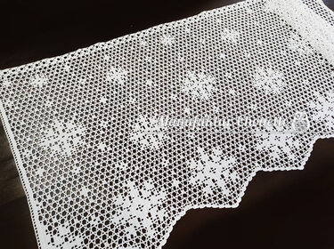 Weiße gehäkelte Spitzenborte im Filethäkelmuster mit Blumenquadraten und gezacktem Rand auf dunklem Untergrund