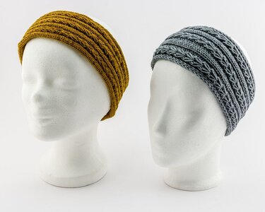 Zwei gestrickte Stirnbänder in Senf und Grau mit Zopfmuster auf Schaufensterköpfen