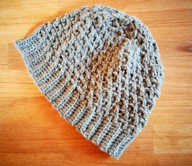 Graue gehäkelte Mütze mit geripptem Bündchen und Strukturmuster auf Holz