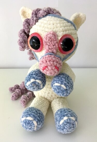 Gehäkeltes Einhorn-Amigurumi in Creme mit lila Mähne und hellblauen Hufen, sitzend