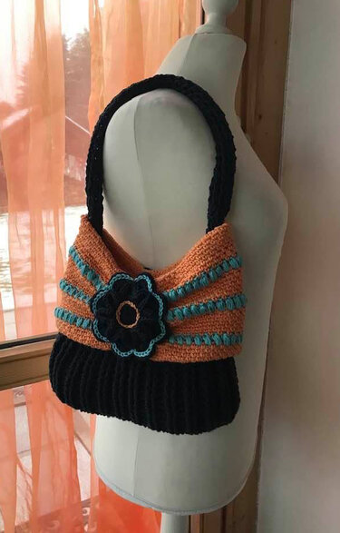 Gehäkelte Umhängetasche in Orange, Schwarz und Türkis mit Häkelblume an einer Schneiderbüste