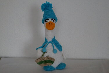 Weiß gehäkelte Amigurumi-Gans mit orangefarbenem Schnabel, türkisfarbener Mütze, Schal und Korb