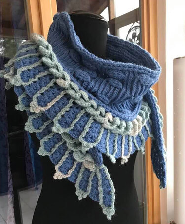 Gehäkeltes blaues Dreieckstuch mit schuppenartigem Relief auf einer schwarzen Schneiderpuppe.