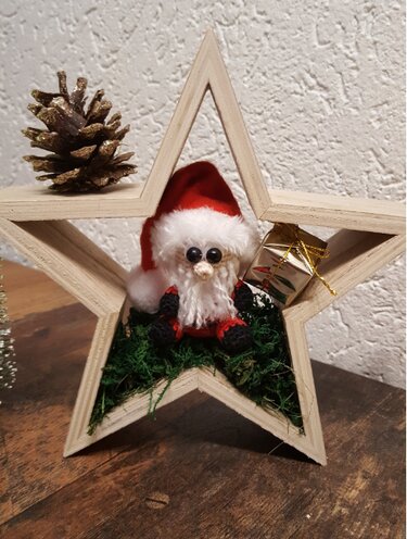 Gehäkelter Weihnachtsmann-Amigurumi in Holzstern mit Moos, Geschenk und Tannenzapfen als DIY-Dekorationsidee