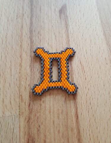 Perlen-Anhänger Sternzeichen Zwillinge in Orange und Grau auf hellem Holz