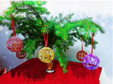 Vier schnell gehäkelte Weihnachtskugeln in verschiedenen Farben an roten Bändern an einem Tannenzweig