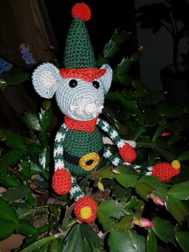 Gehäkelte Amigurumi-Maus in grüner Kleidung mit rotem Schal und Zipfelmütze, sitzend auf einem Weihnachtskaktus