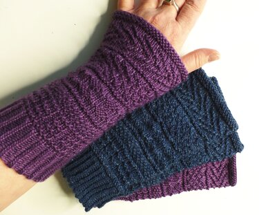 Zwei gestrickte Armstulpen in Lila und Dunkelblau, eine am Handgelenk getragen, mit Rippenmuster.