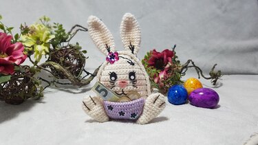 Gehäkelter Amigurumi-Osterhase mit lila Körbchen für Geldschein und Münzen, daneben bunte Ostereier