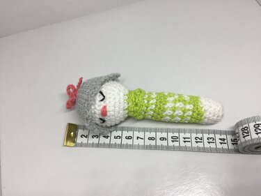 Handgehäkelte Baby-Rassel mit grauer Mütze, grün-weißem Griff und Maßband