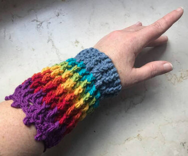 Fingerlose gehäkelte Armstulpe mit grauem Bündchen und mehrfarbigem Zackenrand