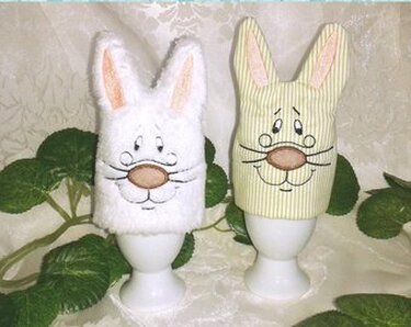 Zwei Hasen-Eierwärmer (weiß und grün-gestreift) auf Eierbechern