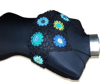 Gehäkeltes schwarzes Crop-Top mit blauen und grünen Blumen-Granny-Squares auf schwarzer Büste.