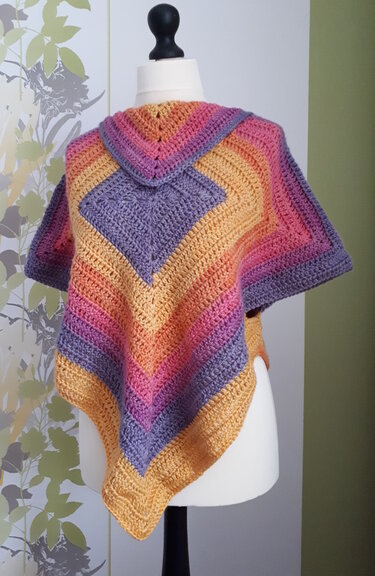 Gehäkelter Poncho in Lila, Pink, Orange und Gelb mit Rautenmuster auf einer Schneiderpuppe.