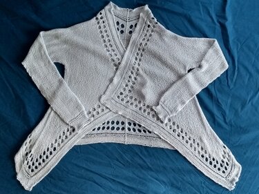 Hellgraue offene Damenstrickjacke mit Lochmuster auf blauem Untergrund