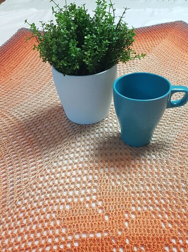 Häkel-Tischläufer in orange-beige mit Topfpflanze und blauer Tasse