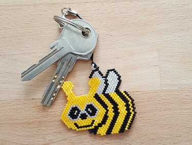 Perlenanhänger in Bienenform neben zwei Metallschlüsseln auf Holzoberfläche
