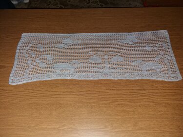 Rechteckiger gehäkelter Tischläufer in Hellgrau mit Elchmotiven auf Holzoberfläche.