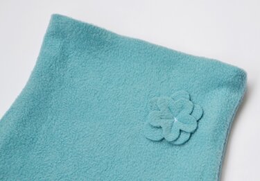 Detail eines türkisfarbenen Fleece-Loops mit gestapelter Blütenapplikation und abgestepptem Saum