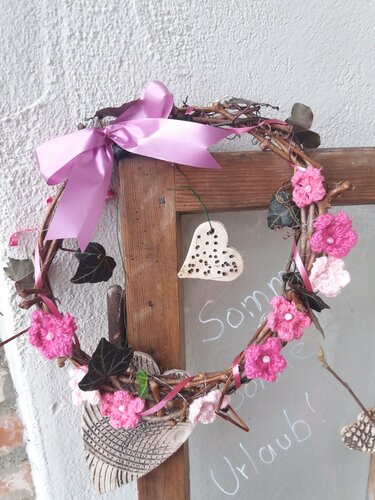 Zweigkranz mit rosa gehäkelten Blumen, grünen Blättern, rosa Schleife und kleinen Keramikherzen.