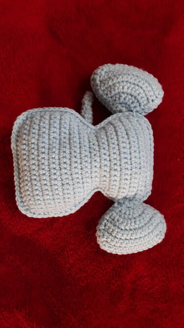 Gehäkelte Einzelteile eines Amigurumi-Elefanten (Kopf und zwei Ohren) aus hellgrauem Garn auf rotem Stoff.