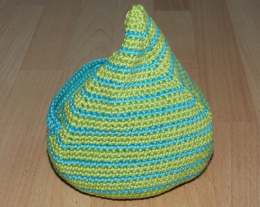 Gehäkeltes konisches Objekt mit hellgrünen und türkisen Streifen auf Holzuntergrund
