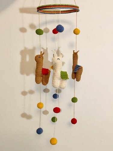 Gehäkeltes Mobile mit drei Lama-Figuren und bunten Häkelkugeln an einem regenbogenfarbenen Ring.
