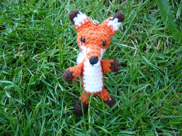 Handgehäkelter Fuchs-Amigurumi in Orange und Weiß mit Schlüsselring auf Gras.