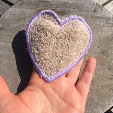 Herzförmiger Untersetzer mit lila Stickrand auf einer offenen Hand