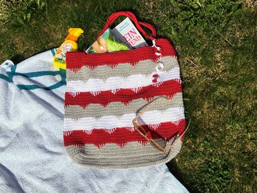 Gehäkelter Shopper in Rot, Weiß und Grau mit Wellenmuster auf Handtuch im Gras