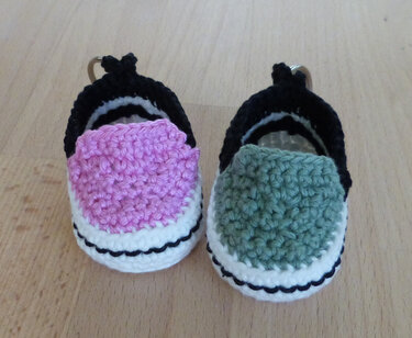 Zwei gehäkelte Mini-Sneaker-Schlüsselanhänger in Rosa und Grün auf Holzuntergrund