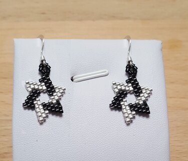 Zwei sternförmige Ohrringe aus schwarzen und silbernen Rocaillesperlen auf weißem Display