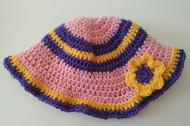 Gehäkelte Babymütze rosa mit lila und gelben Streifen und gelber Blumenapplikation