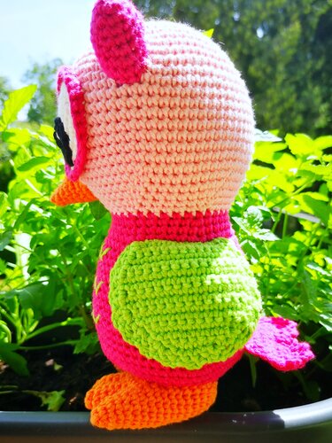 Seitenansicht einer gehäkelten Amigurumi-Eule in Rosa und Pink mit grünen Flügeln und orangen Füßen im Pflanztopf.