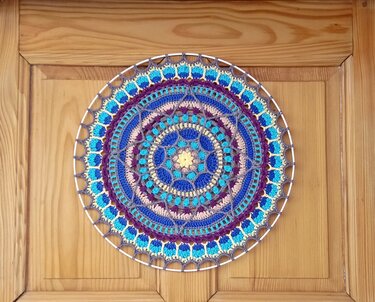 Gehäkeltes rundes Mandala auf Metallring vor Holztür mit Detail der Maschen