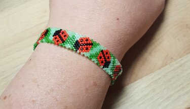 Gefädeltes Perlenarmband mit roten Marienkäfern am Handgelenk