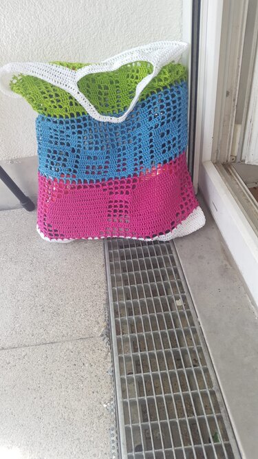 Gehäkelte Tasche mit grünen, blauen und pinken Streifen und weißem Rand neben einer Türöffnung