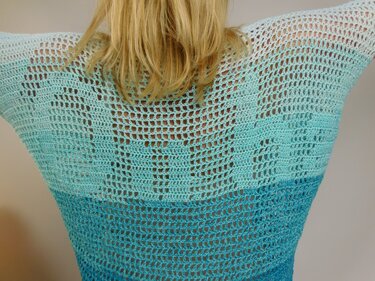 Rücken einer Person mit hell‑ bis dunkel­türkis gehäkelter Tunika im offenen Netzmuster