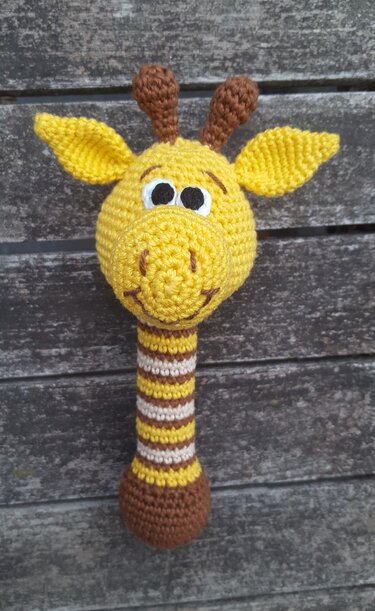 Gehäkelte Giraffenrassel in Gelb mit gestreiftem Griff auf Holzuntergrund.