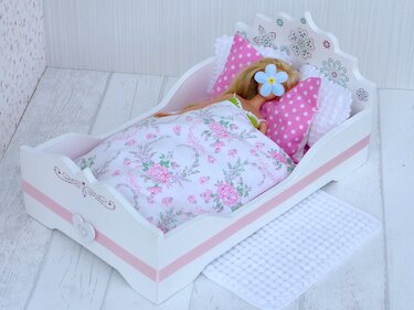 Puppe liegt in einem weißen Holz-Puppenbett mit rosa Streifen, geblümter Decke und rosa gepunkteten Kissen